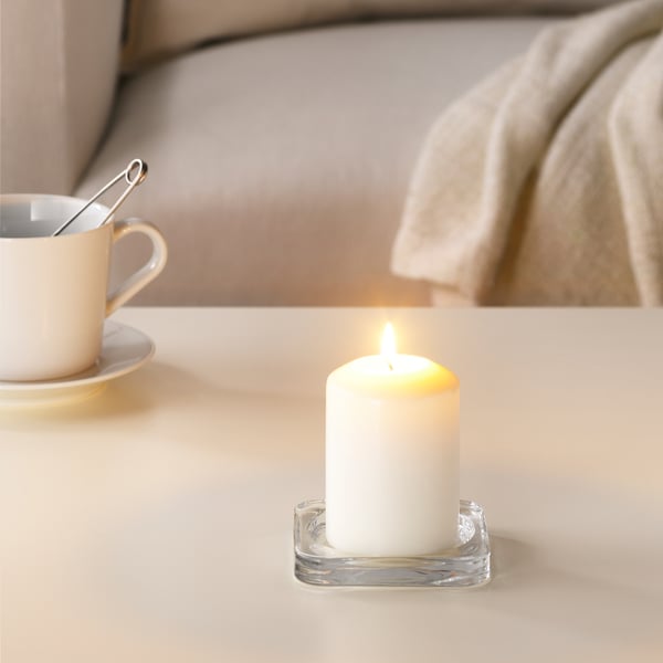 Lit white candle in clear holder beside white coffee cup, creating cozy atmosphere.