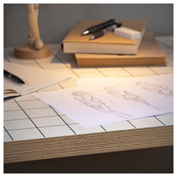 Square white desk with sketches, books, and pen. Desk has pre-drilled holes and plywood edge.