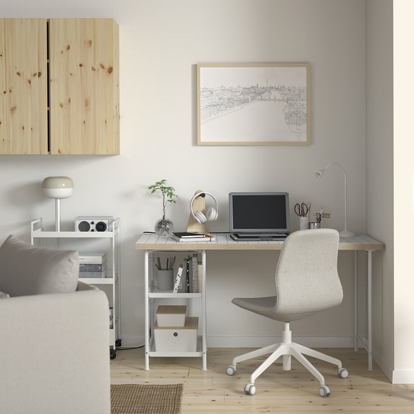 Home office setup with LAGKAPTEN desk, white, wooden top, grey chair, against light wall. Art print above, speakers left, plant center.