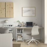 Home office setup with LAGKAPTEN desk, white, wooden top, grey chair, against light wall. Art print above, speakers left, plant center.
