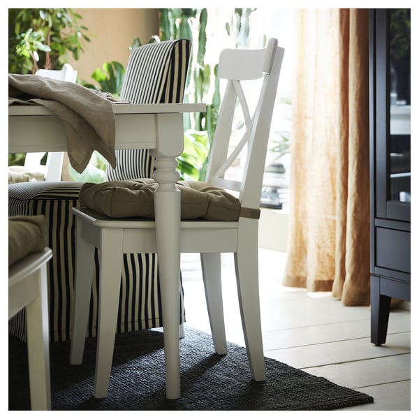 White wooden chairs with beige cushions and striped fabric seats are positioned near a window on a dark blue jute rug.