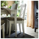 White wooden chairs with beige cushions and striped fabric seats are positioned near a window on a dark blue jute rug.