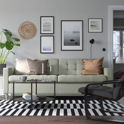 Modern living room with green LANDSKRONA sofa, black-and-white rug, art wall, and coffee table with books and cup.