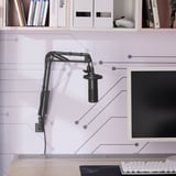 A desk setup with a microphone arm mounted to the desk, holding a microphone near a computer monitor.