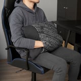 Person sitting in an office chair, holding a multi-functional cushion designed for lumbar support, warmth, and versatility.