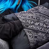 Person in blue hair, wearing black LÅNESPELARE cushion blanket with geometric design.
