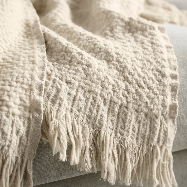 Textured off-white throw blanket with fringed edges, showcasing handwoven quality and natural fabric.