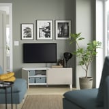 Modern living room with flat-screen tv on sleek media stand. Grey walls, blue couch, and houseplant. Three black-and-white framed photos hang above.