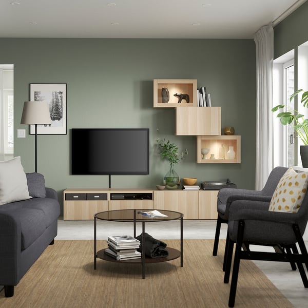 Modern living room with LAPPVIKEN light oak shelves, tv, gray sofa, and round coffee table. Green wall, white curtains, and large window.