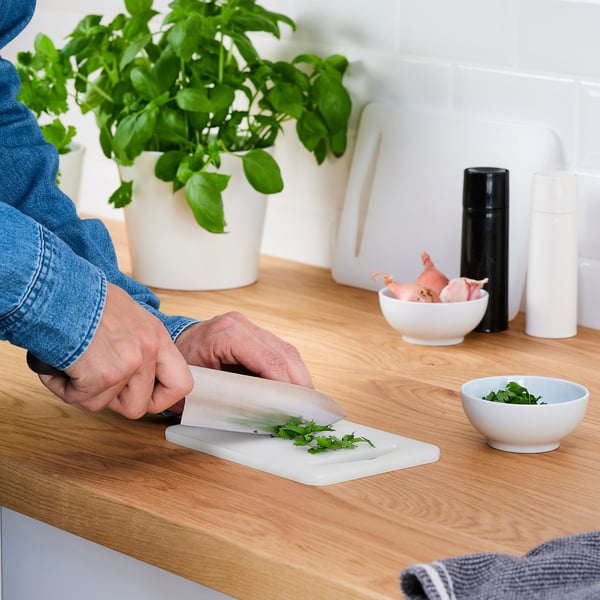 Person chops herbs on LEGITIM plastic chopping board, suitable for various foods and knives.