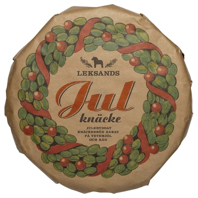 A festive wreath with berries decorates this round, LEKSANDS KNÄCKEBRÖD packaging, a traditional swedish food item.