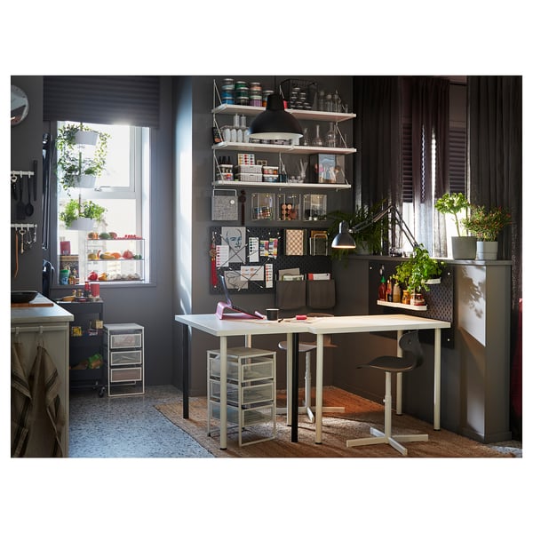 Office space with white table, black chairs, and shelves against dark wall, near window with plants.