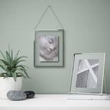 Metal picture frames: one with b&w photo, below abstract shapes. With succulent and stones.