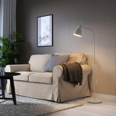 Living room with LERSTA lamp, sofa, pillows, blanket, artwork, plant, dark curtains.