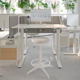 Modern office setup with white LIDKULLEN stool, adjustable height desks, grey dividers, and multiple potted plants for decoration.