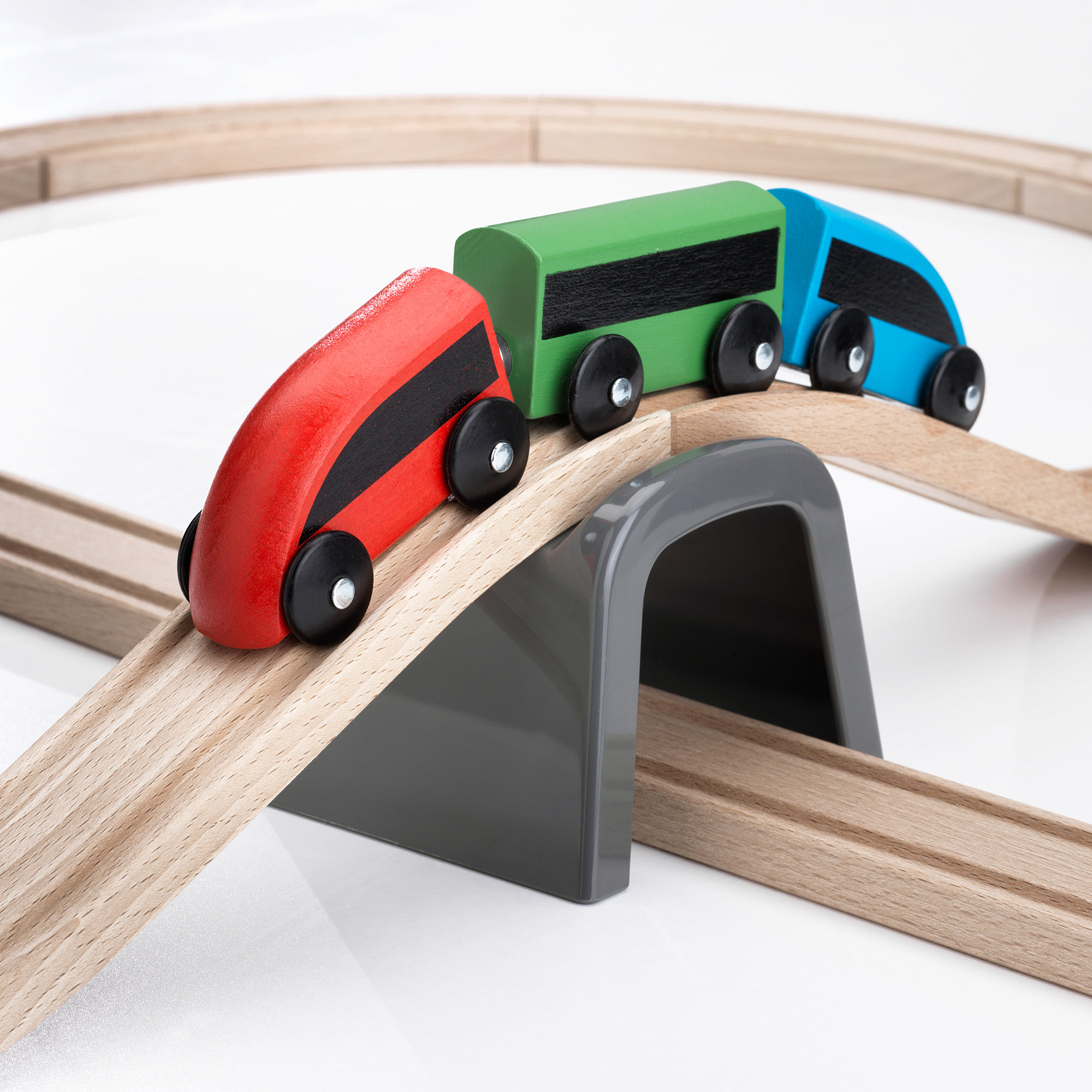 High-quality wooden train set featuring vibrant red, green, and blue cars on tracks, passing through a gray tunnel.