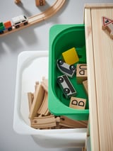 Plastic toy storage container, green and white, holding wooden train tracks and cars.