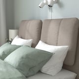 Modern bed with sloped headboard, cushions, white lights, and green bedding.