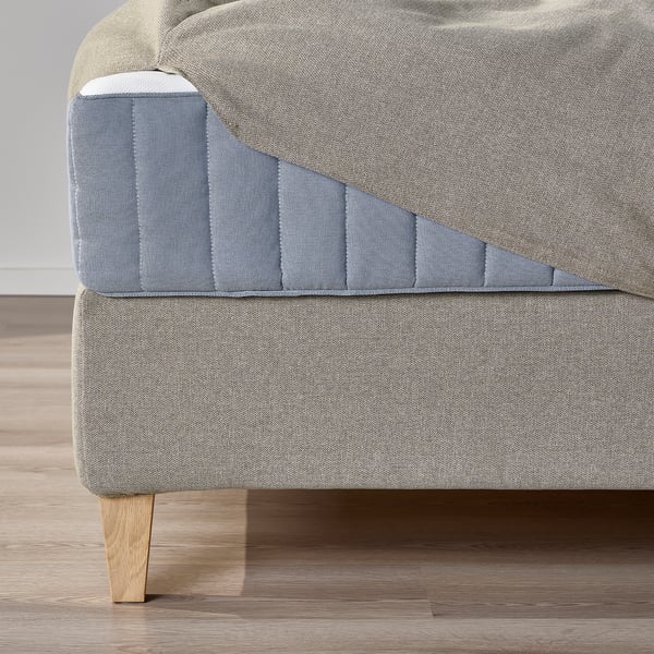 Close-up of upholstered divan bed base, showing sloped headboard and wooden legs.