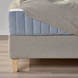 Close-up of upholstered divan bed base, showing sloped headboard and wooden legs.