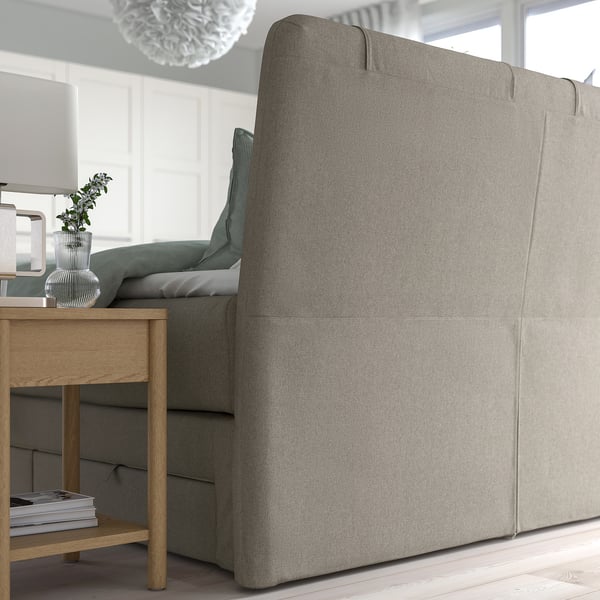 Modern grey upholstered bed with sloped headboard by large window. Includes cushions and storage drawers underneath.