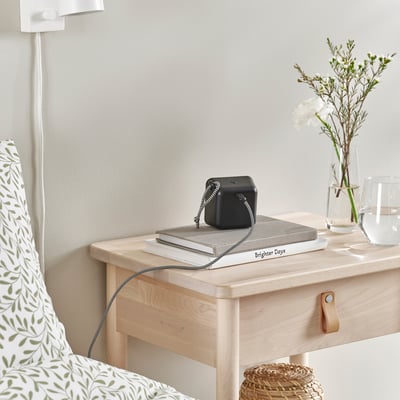 Black cube-shaped usb cable organizer on nightstand, with a stack of books and flowers.
