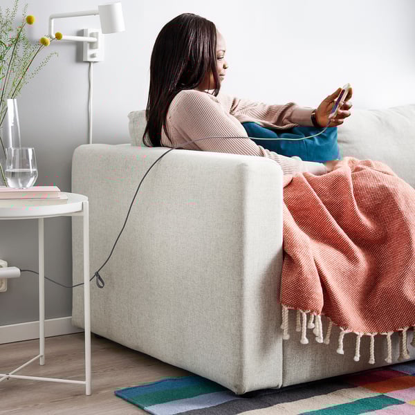 Person on couch using smartphone, pink blanket, flowers, glass, adjustable lamp.