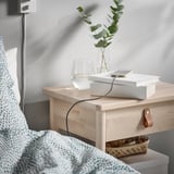 Bedside setup: booked with wooden nightstand, charging phone with LILLHULT usb cable, water glass, book, and plant.