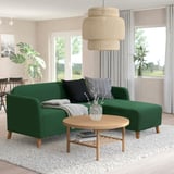 Green LINANÄS sofa with black and gray pillows, wooden round coffee table, magazines, and a large natural pendant light above.