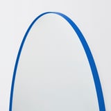 A large, elegantly curved mirror with a sleek blue frame is mounted on a wall. The high-quality design adds depth and sophistication to the space.