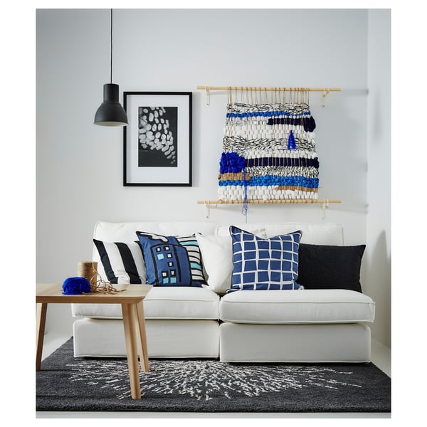 Modern living room with white LISABO sofa, blue and black pillows, hanging rope art, gray rug, and wood coffee table under black pendant lamp.
