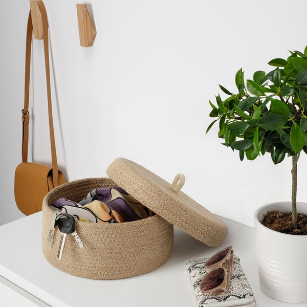 Woven basket with lid holding keys and accessories, beside potted plant.