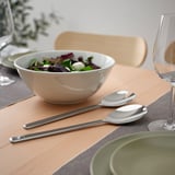 Modern, elegant table setting with LÖFTESRIK cutlery; silver steel, round handles; bowl of salad beside; wine glasses nearby.