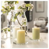 White candles in glass holders beside clear vase with flowers.