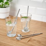 Glasses of water with ice, mint, and straws, plus cleaning brush and spoon straws on wood.