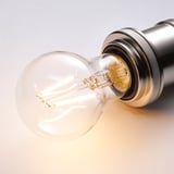 A close-up of a clear led bulb with a twisted filament, emitting warm white light, placed in a metallic holder.