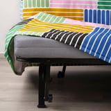 Bed with colorful, striped quilt and grey mattress on black metal base with wheels.