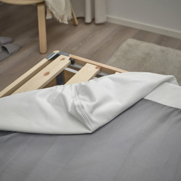 Bed base with removable white cover, supported by wooden slats, showing its functionality and design.