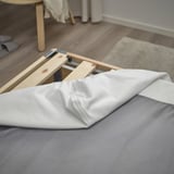 Bed base with removable white cover, supported by wooden slats, showing its functionality and design.