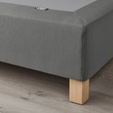 Image depicts corner of grey upholstered bed base on wooden floor, showing flat slats and burfjord oak legs, offering support and easy transport.