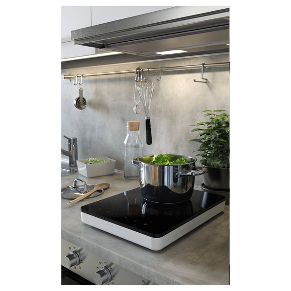 Modern kitchen with stove, veggies, utensils, plants.