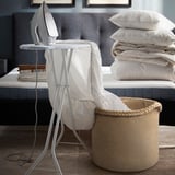 White ironing board with garment in bedroom, jute basket with blankets.