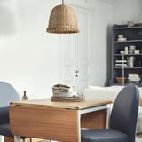MÄVINN lamp in banana fiber hangs, lighting simple dining area with wooden table and grey chairs, creating cozy, rustic atmosphere.