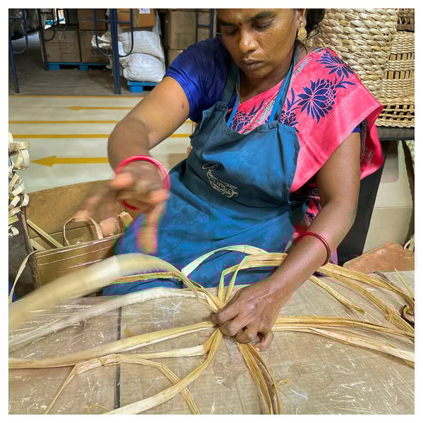 Woman weaving banana fiber lamp in workshop.