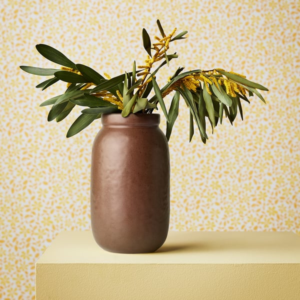 Vase displays flowers on stand against patterned wall.