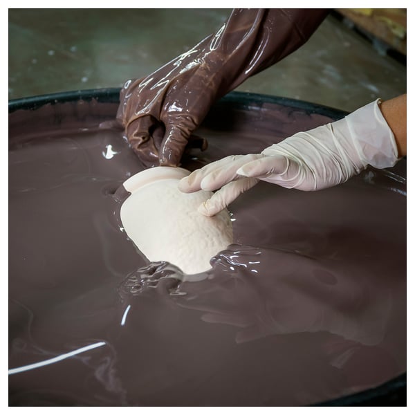 Empty-handed person dips gloved hand into chocolate bath.