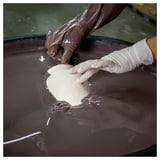 Empty-handed person dips gloved hand into chocolate bath.