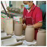 Person crafting earthy-toned, hand-shaped, minimalist MÄVINN vase from stoneware in a workshop.