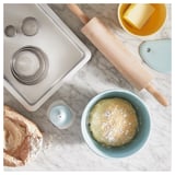 A baking setup featuring tools like a rolling pin, bowls with dough and butter, and cookie cutters on a marble countertop.