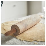 Wooden rolling pin on floured dough.
